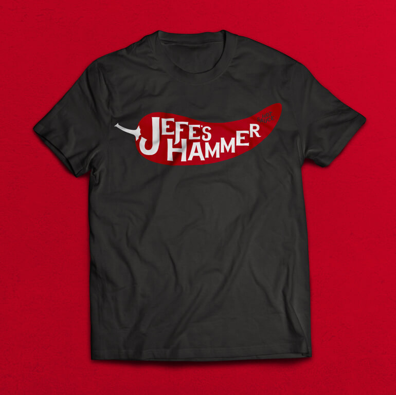 jefes-hammer-tshirtA Black t-shirt with red pepper and white text printed on it, sitting on a red background